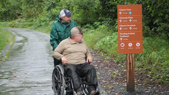 Two people, one in wheelchair, look at directions on sign