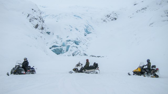 Three snowmobiles in front of a snow-covered glacier