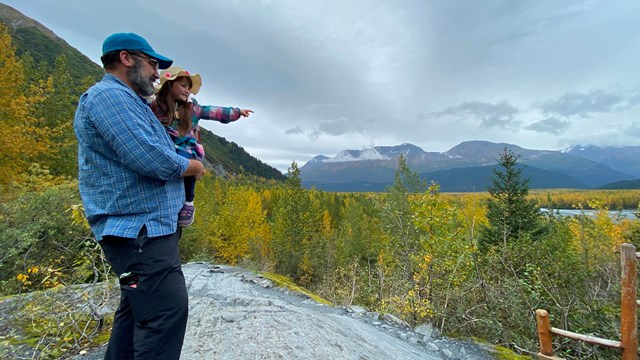 A person holding a small child pointing to distance with a green valley beyond.