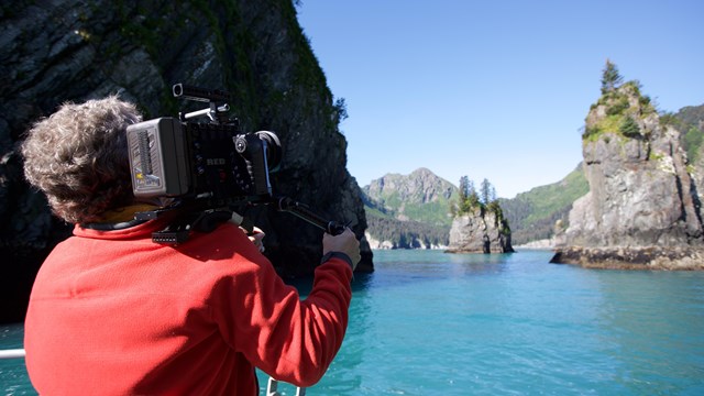 A person films spire-like rocks in turquoise waters
