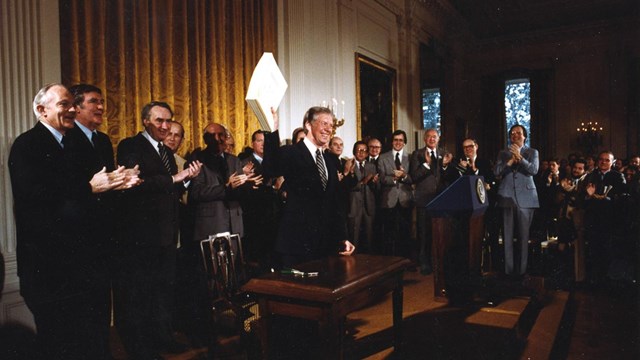 President Jimmy Carter holds up signed papers in front of a clapping audience
