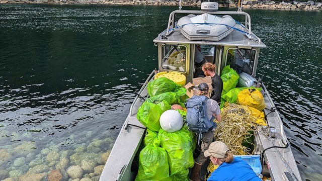 Three people load bags of trash onto a boat