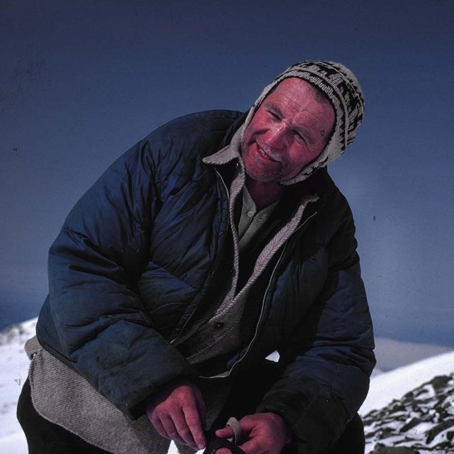 A historic photo of a person in warm clothes from the late 60s stands on the snow. 