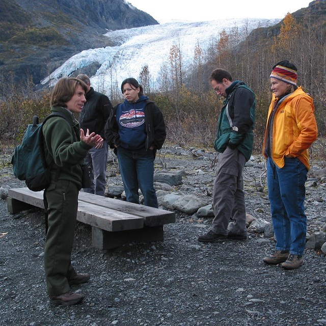 Ranger gestures to a group of adults standing in front of exit glacier. 