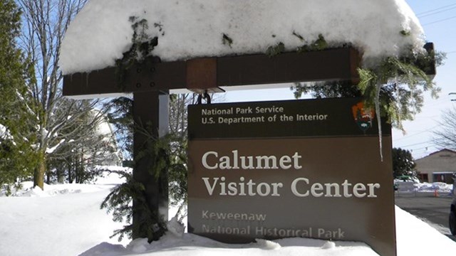 A sign covered on the top with snow reading "Calumet Visitor Center."