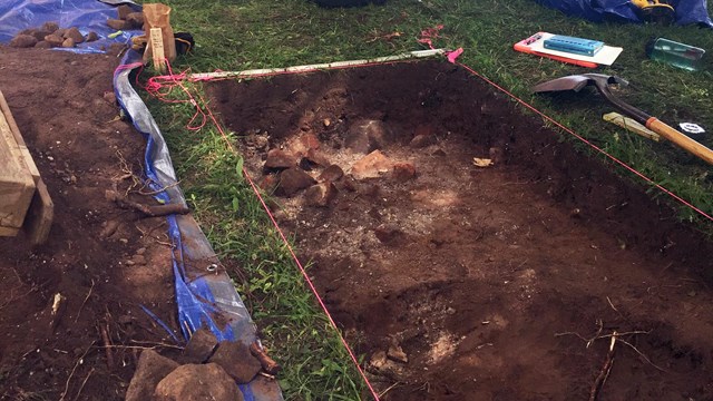 A large rectangular hole in the ground surrounded by tools.