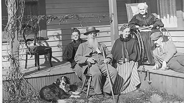 Four people sit on and just off of the front porch of a house.