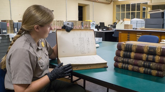 A person with gloves on opens an old book.