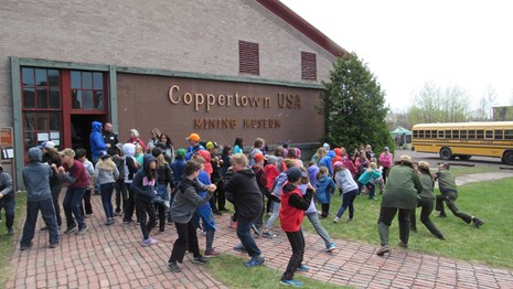 A group of standing students mimic the actions of park rangers on a lawn.