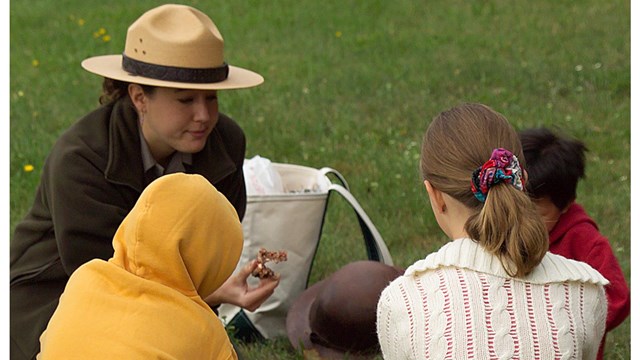 Park ranger working with three children outside. 