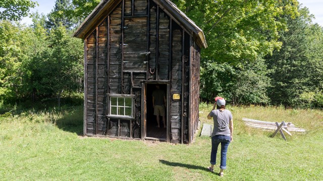 Two people explore an the outside of an old log structure.