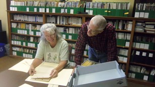 Two volunteers sort through archival materials inside of a library.