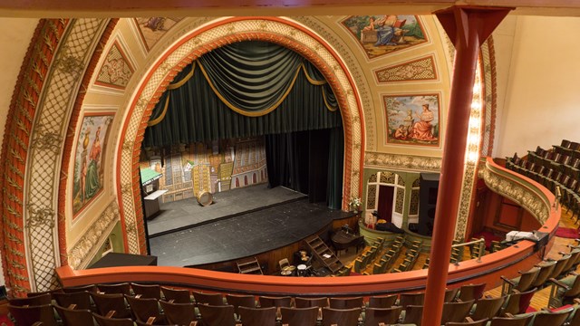 Interior of theatre from second balcony looking down at large stage framed by proscenium arch.