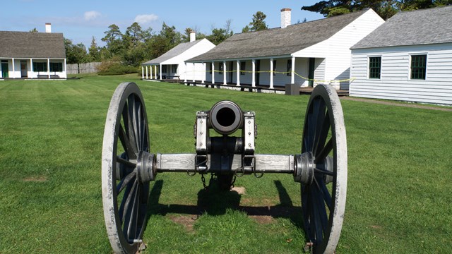 A historic cannon is facing the viewer with buildings in the background.