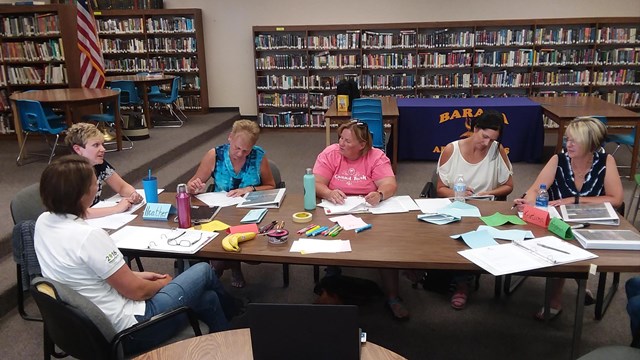 A group of people sit around a table talking and writing on paper.