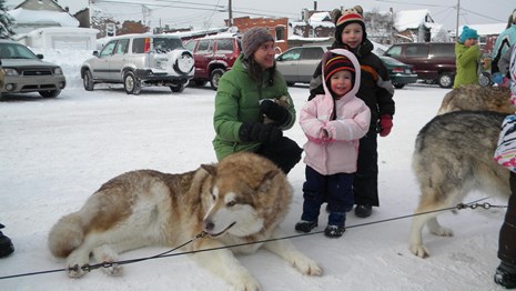 A sled dog lays on the ground and young children stand next to it.
