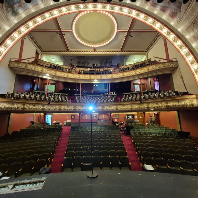 Looking out from a stage toward the seating area. Lights illuminate a half circle overhead.