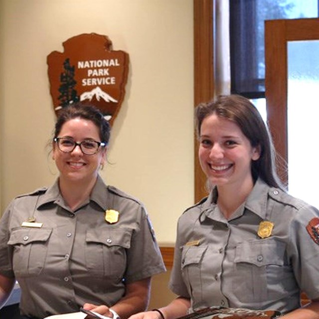 Two park rangers smiling at a park visitor center.