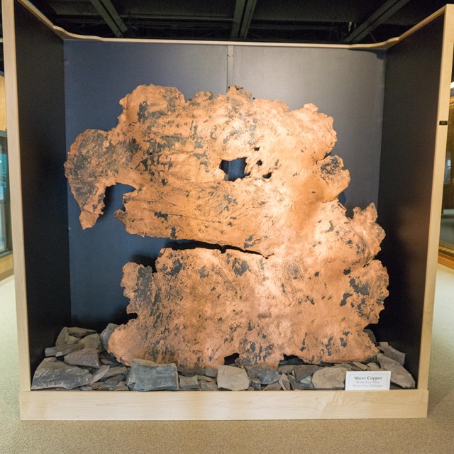 A large piece of flattened orange-colored copper standing upright on display.