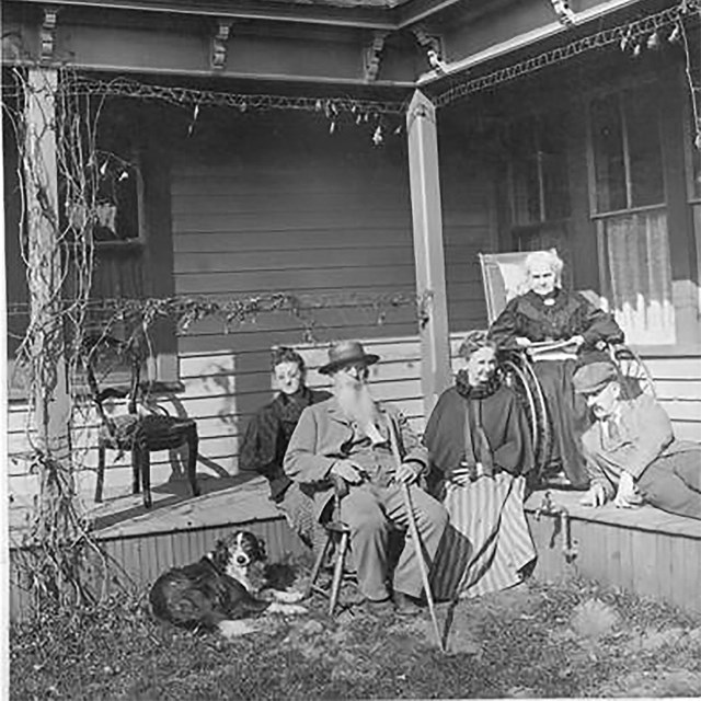 Five people and a dog sitting outside on the front porch of a house.