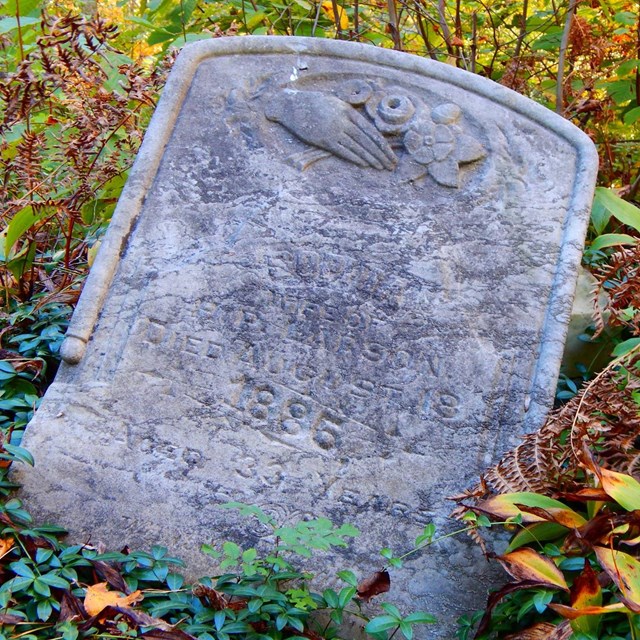 An old grave marker with an unreadable engraving lays in the grass.