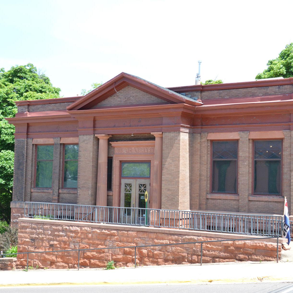 A red brick and stone building sits on a hillside with a street downhill to the left in front.