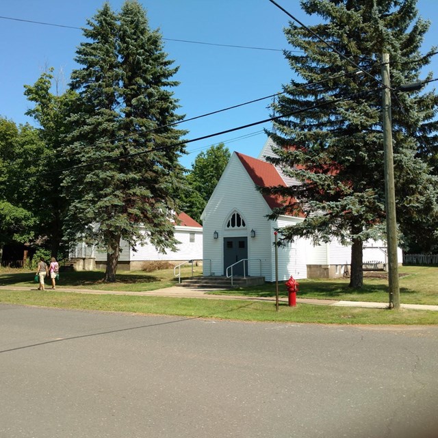 Two buildings with white siding and red roofs surrounded by trees.