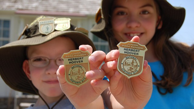 Two kids hold up Junior Ranger badges from Herbert Hoover National Historic Site