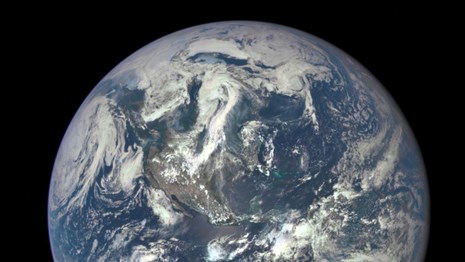 Blue Earth in space with swirling clouds over the western hemisphere.