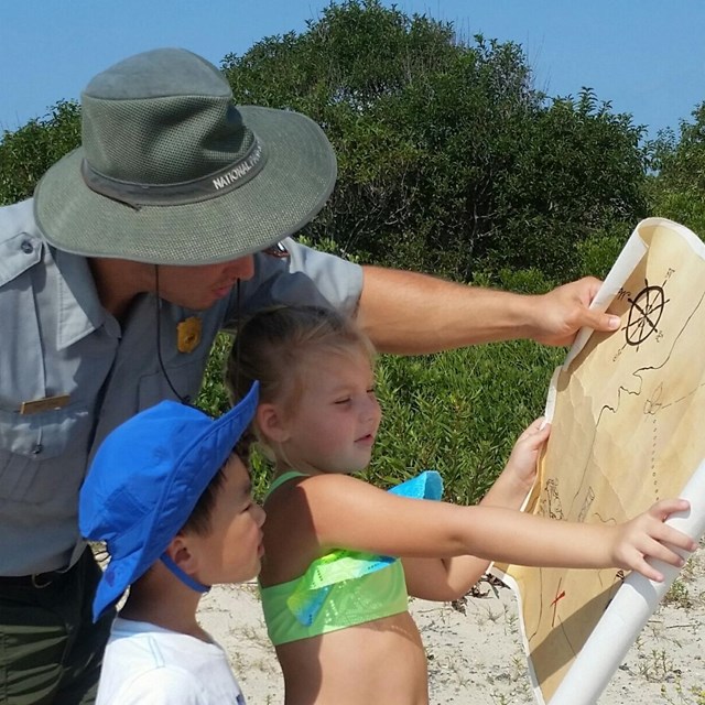A male ranger points at a map while talking to a young boy and girl.