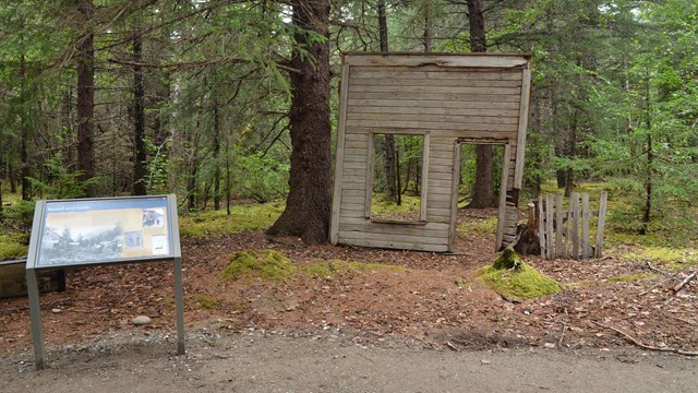 A panel next to an old store front surrounded by trees. 