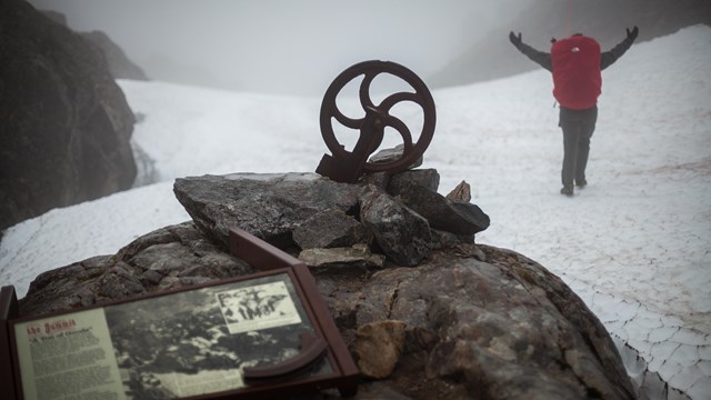 A hiker stands at the summit of the Chilkoot Trail in a mountain pass. 