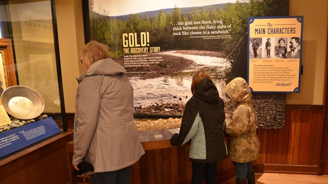 An adult and two children look at an exhibit about gold discovery