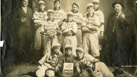 Ten young players and two adults pose with baseball gear and a cigar box.