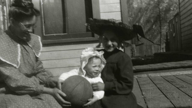 Black and white photo of a woman, a girl, and a baby pose with a basketball.