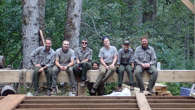 Color modern image of 6 people on a wooden beam, one person stands below