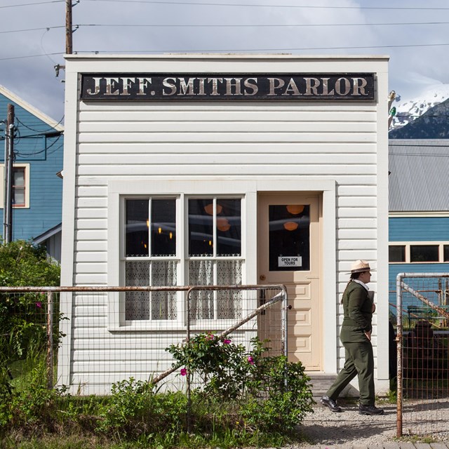 A ranger walks towards people in front of a small, white building