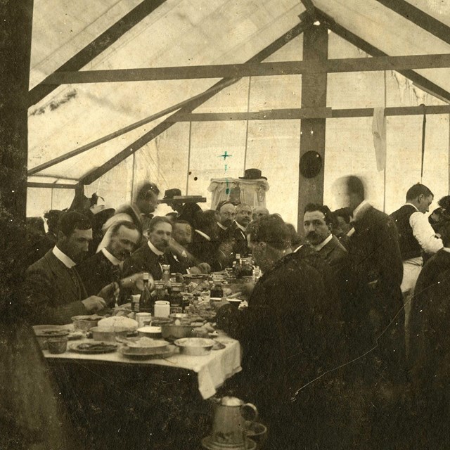 people sit at a long table inside a dining tent