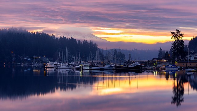 Morning breaks over peaceful Gig Harbor with purple and pink clouds.