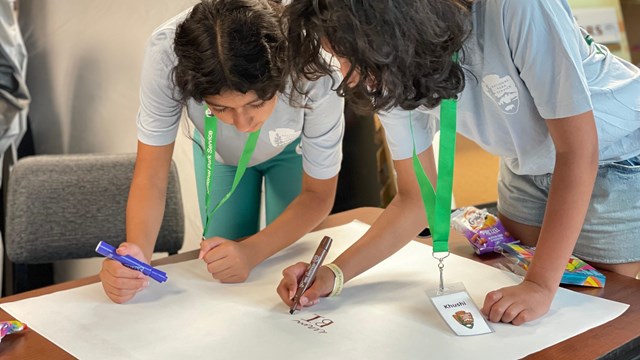 A photograph of two people working together with markers and a big piece of paper.