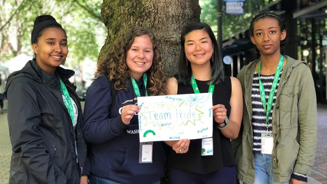 Four people standing together, holding a sign they designed.