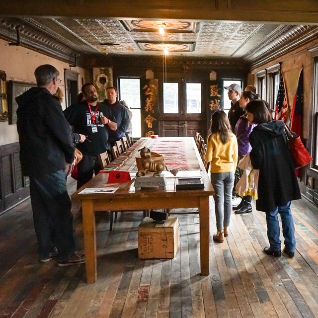 group of people in a long, historic meeting hall gathered around a long table