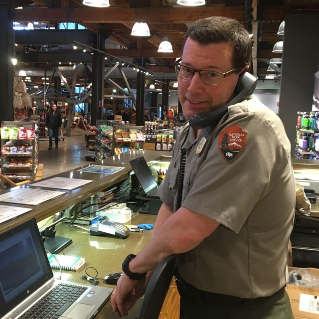 NPS ranger looks directly at viewer while answering phone at a retail desk. 