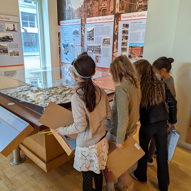 Four children stand next to a table display with clipboards in their hands.