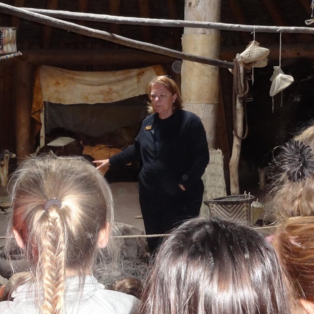 6 students listen to a female ranger's presentation inside an earthlodge.