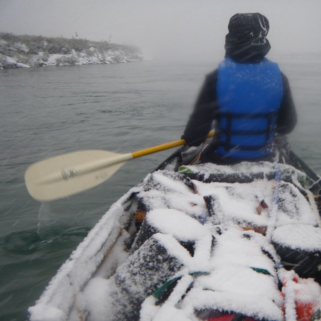 snow rests on the contents of a kayak as man paddles