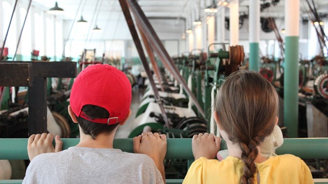 Two kids looking at re-creation of a 1910s mill weaving room.