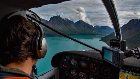 Float plane landing on a blue lake surrounded by steep mountains.