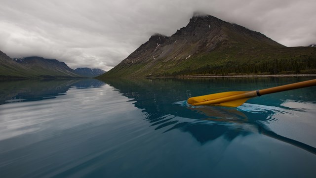 photo of a kayak paddle breaking the water's surface in a blue lake with a mountain in the distance.