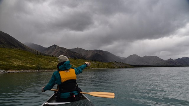 a woman in a canoe points towards a storm ahead
